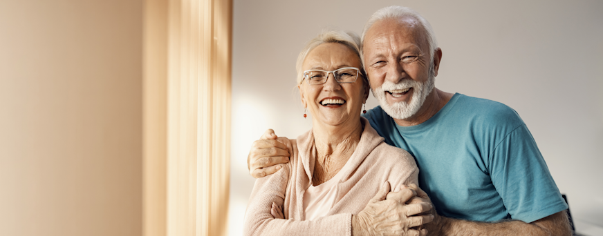 Life Assure Seniors Man And Woman Standing By Window Hero